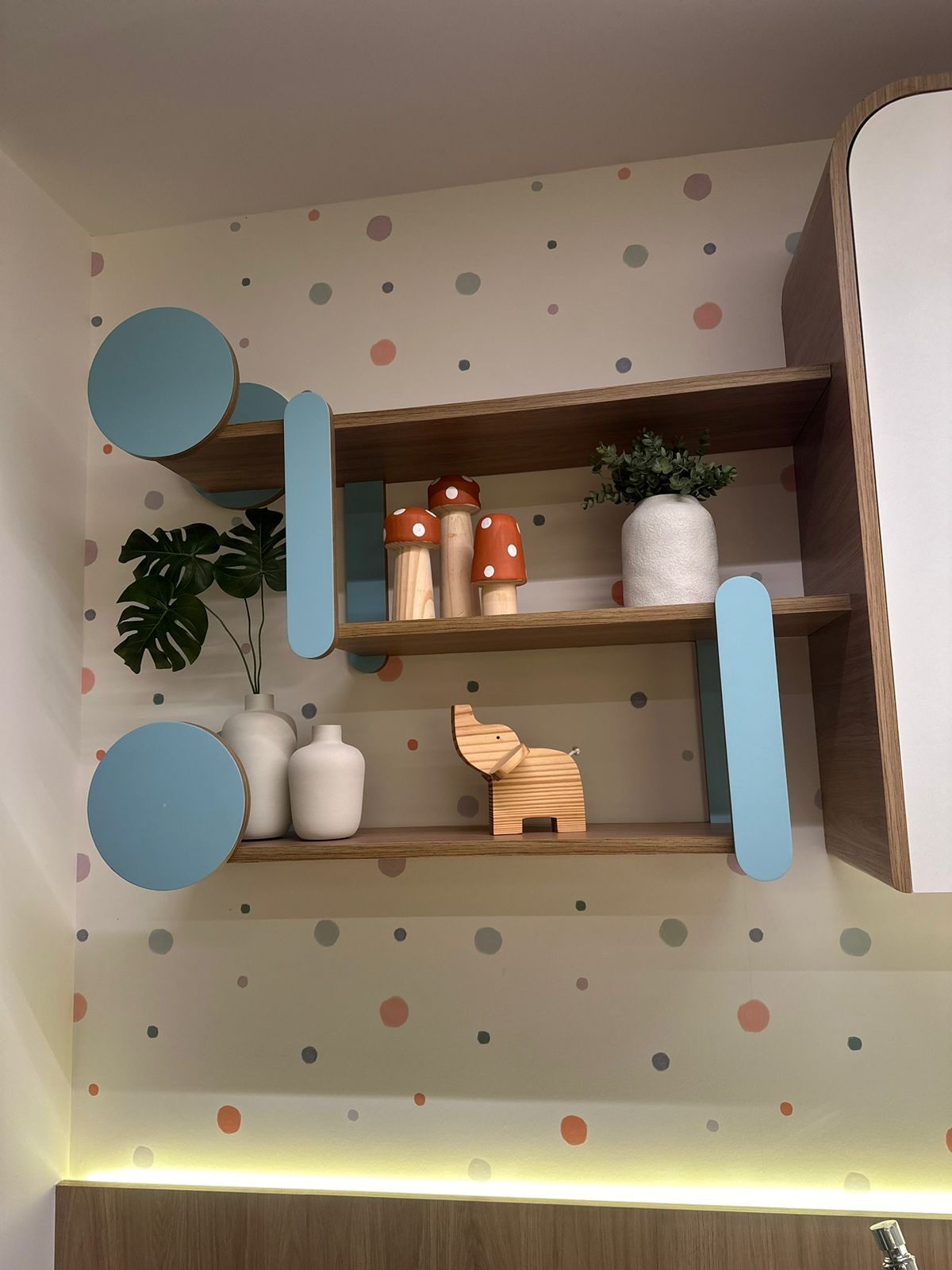 Detalhe de prateleira com objetos decorativos, vegetação e painel de bolinhas coloridas