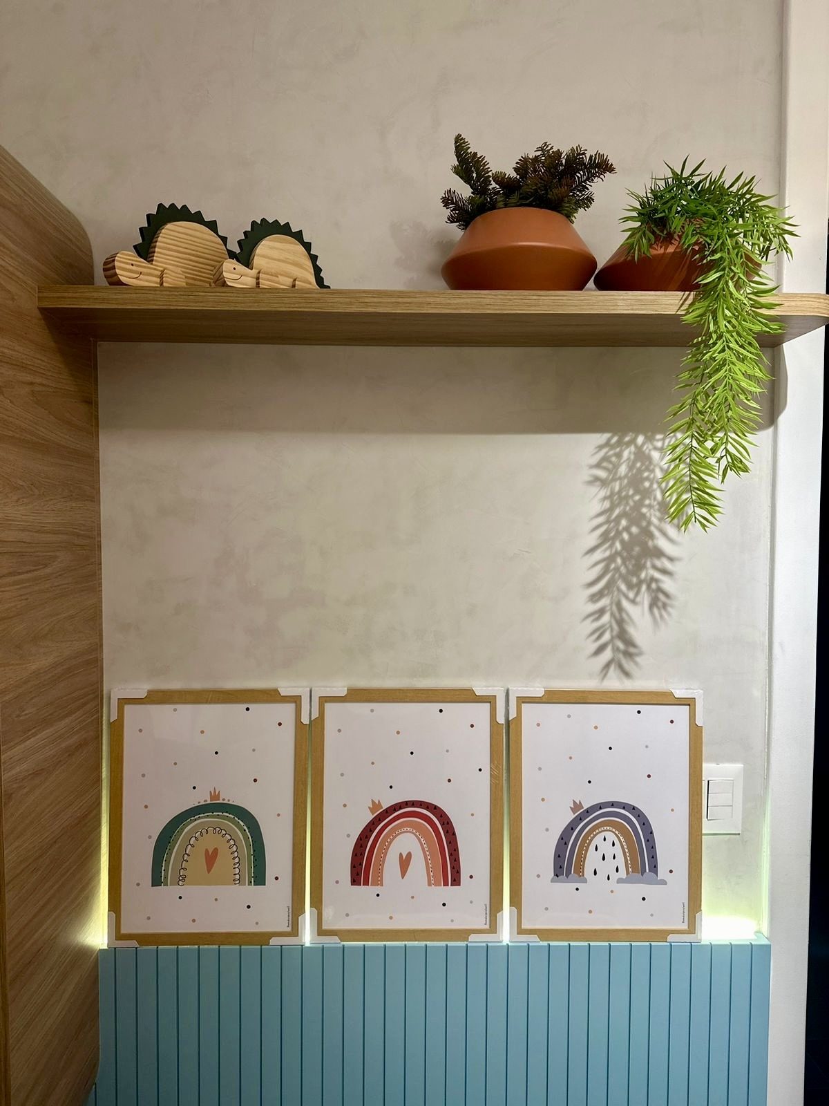 Parede com quadros de arco-íris sobre revestimento de bolinhas e prateleira de madeira com vasos