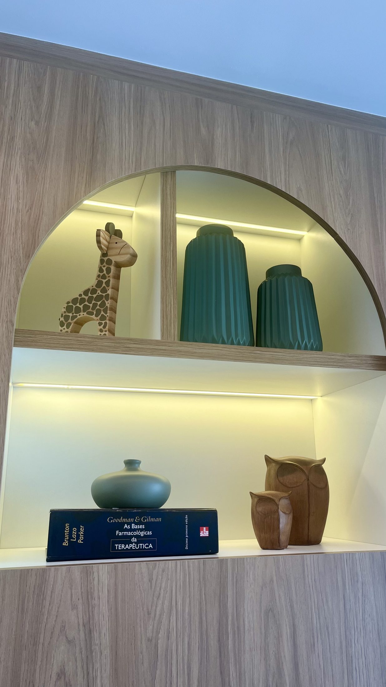 Prateleira iluminada com peças em cerâmica, escultura de girafa e objetos em tons de verde