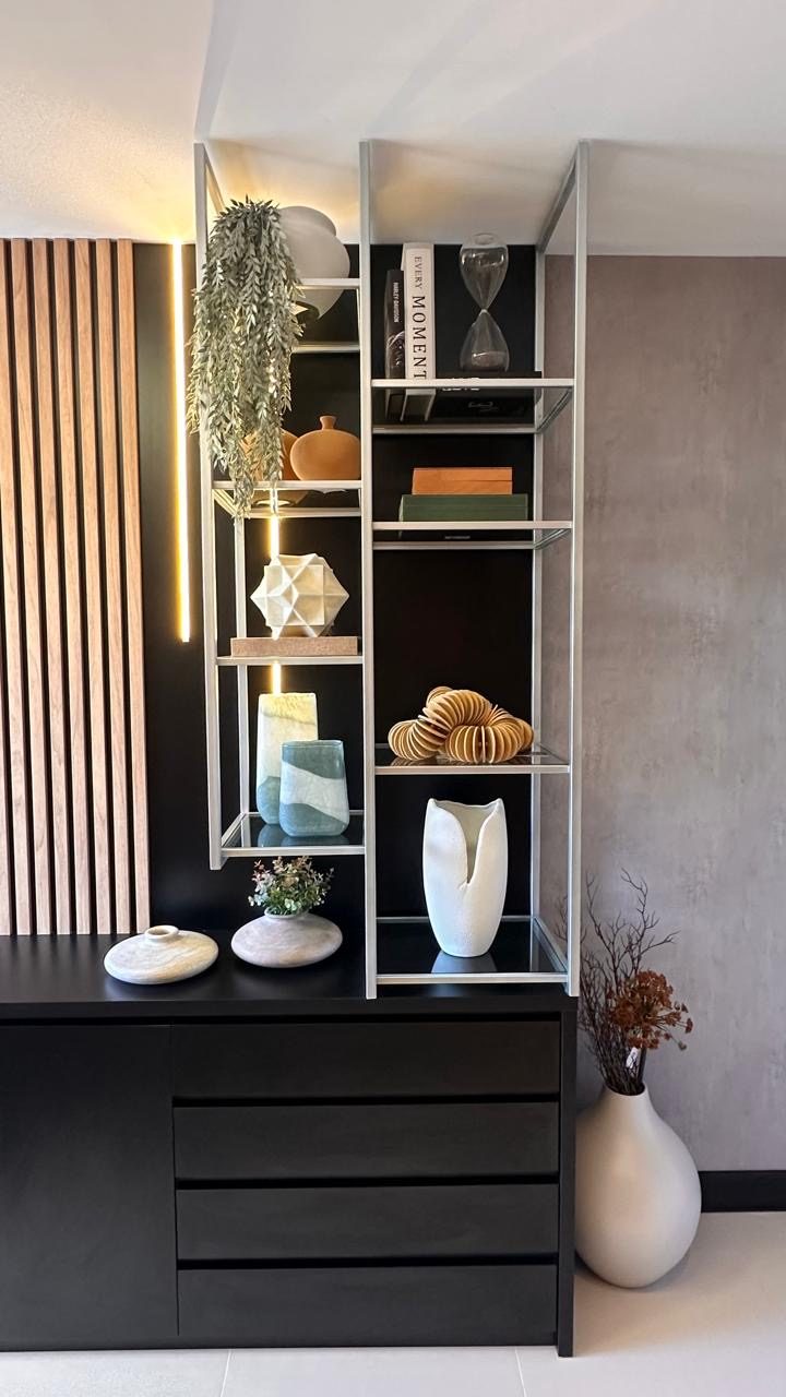 Estante com vasos em cerâmica, livros e gaveteiro preto sob painel de madeira