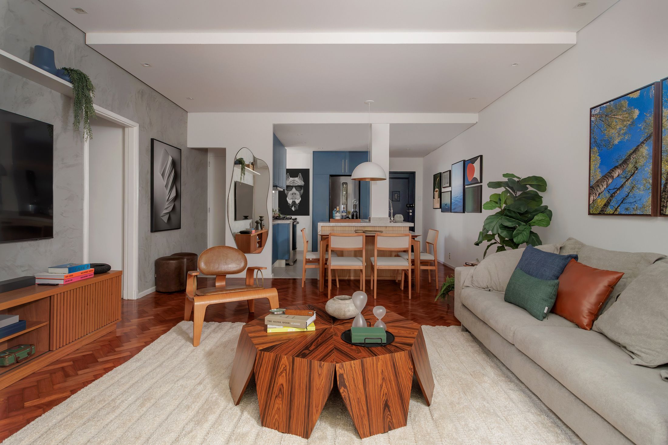 Sala de estar integrada produzida pela Loggia Mobili, com sofá cinza, mesa de centro facetada de madeira e sala de jantar ao fundo