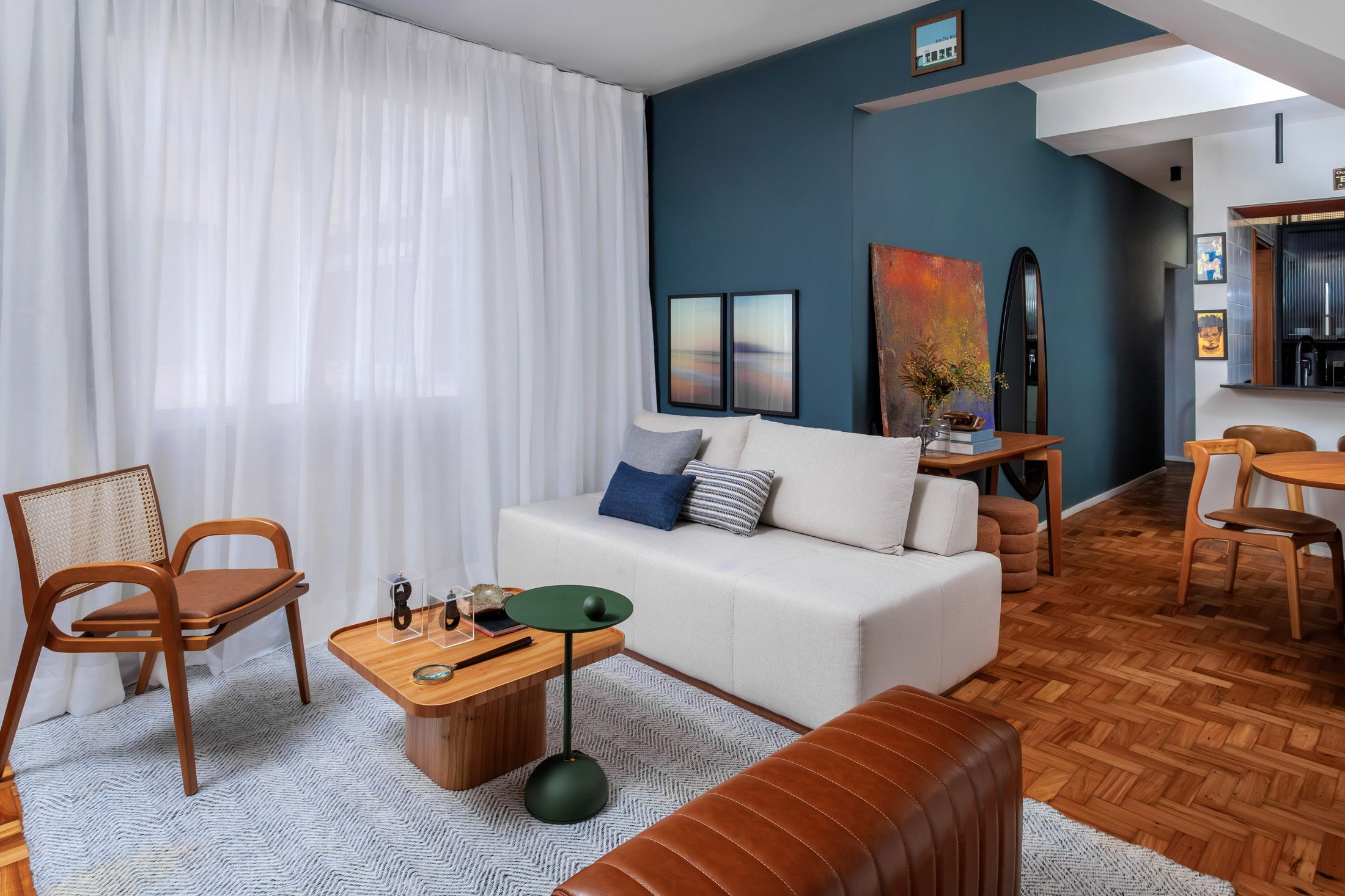 Sala de estar com parede azul profundo, sofá branco e poltrona de madeira, produzida pela Loggia Mobili